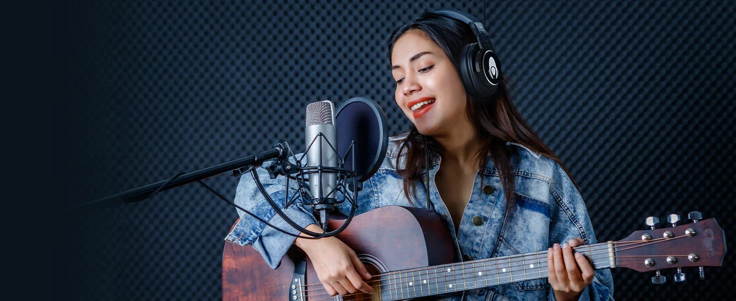A young woman wearing a denim jacket and black headphones sings into a professional studio microphone while playing an acoustic guitar. The background features a soundproofed studio wall, and the "TALOMEN" logo is visible in the top right corner.